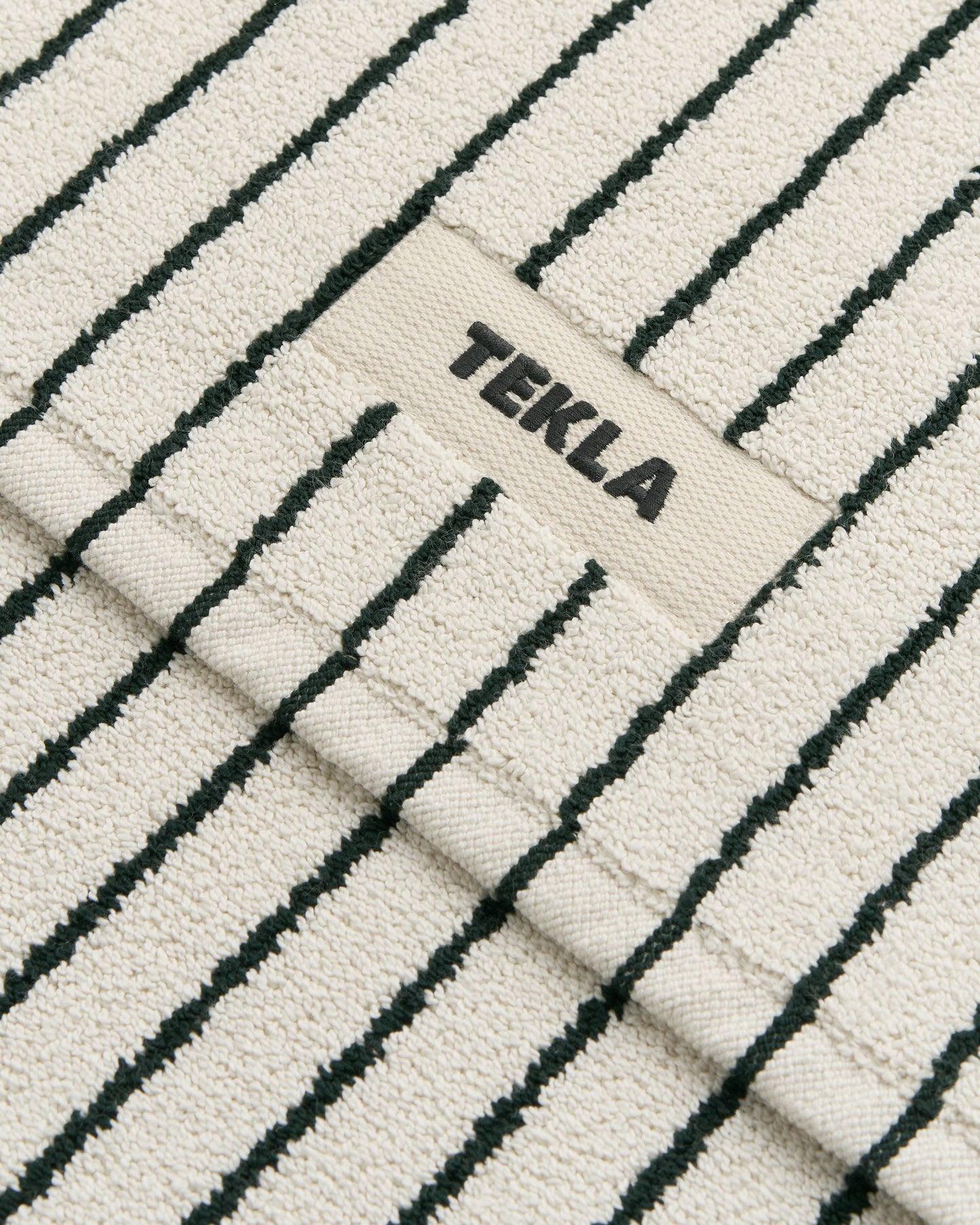 Textured fabric with black stripes and 'TEKLA' branding.