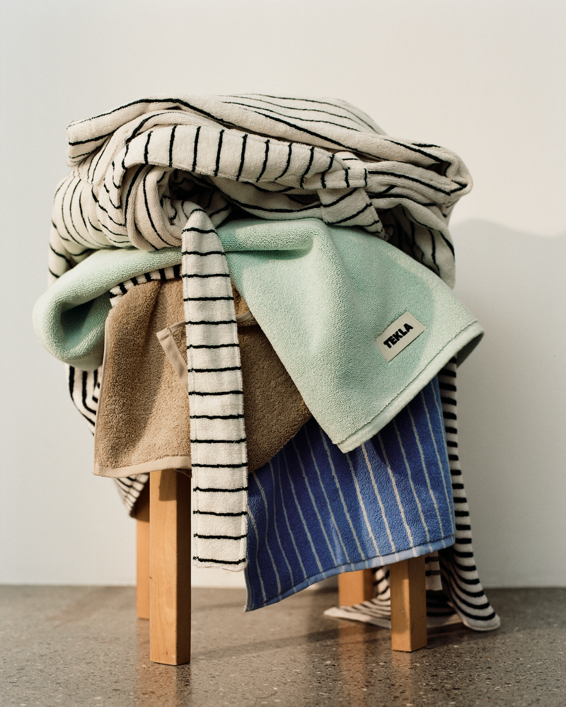 Stack of folded blankets on a wooden stool with a plain background