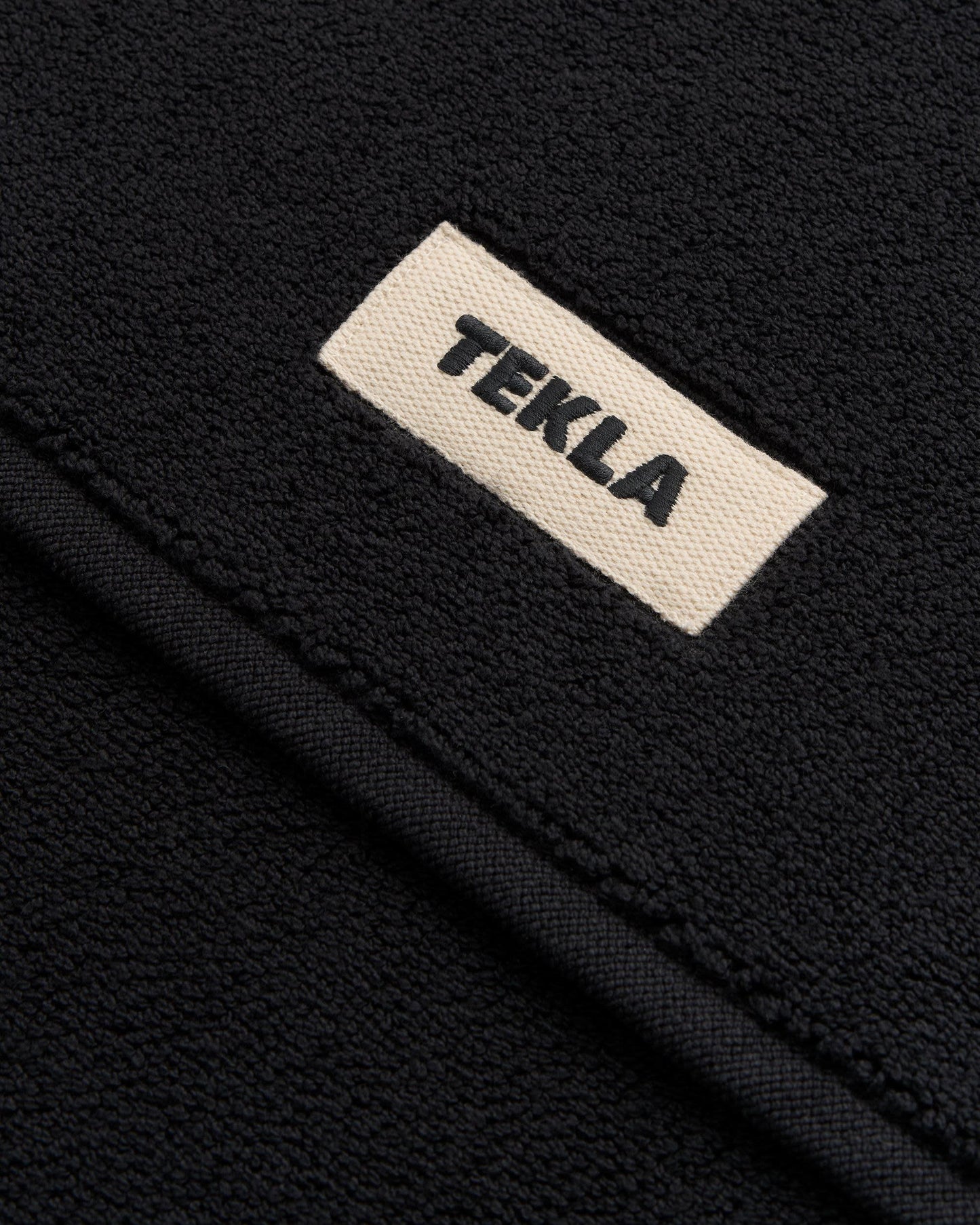 Close-up of a black fabric surface with a beige label displaying the brand 'Tekla'.