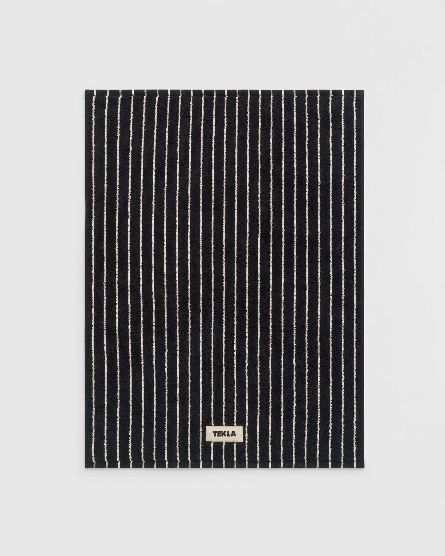 Black and white striped towel with 'Tekla' label on a light gray background