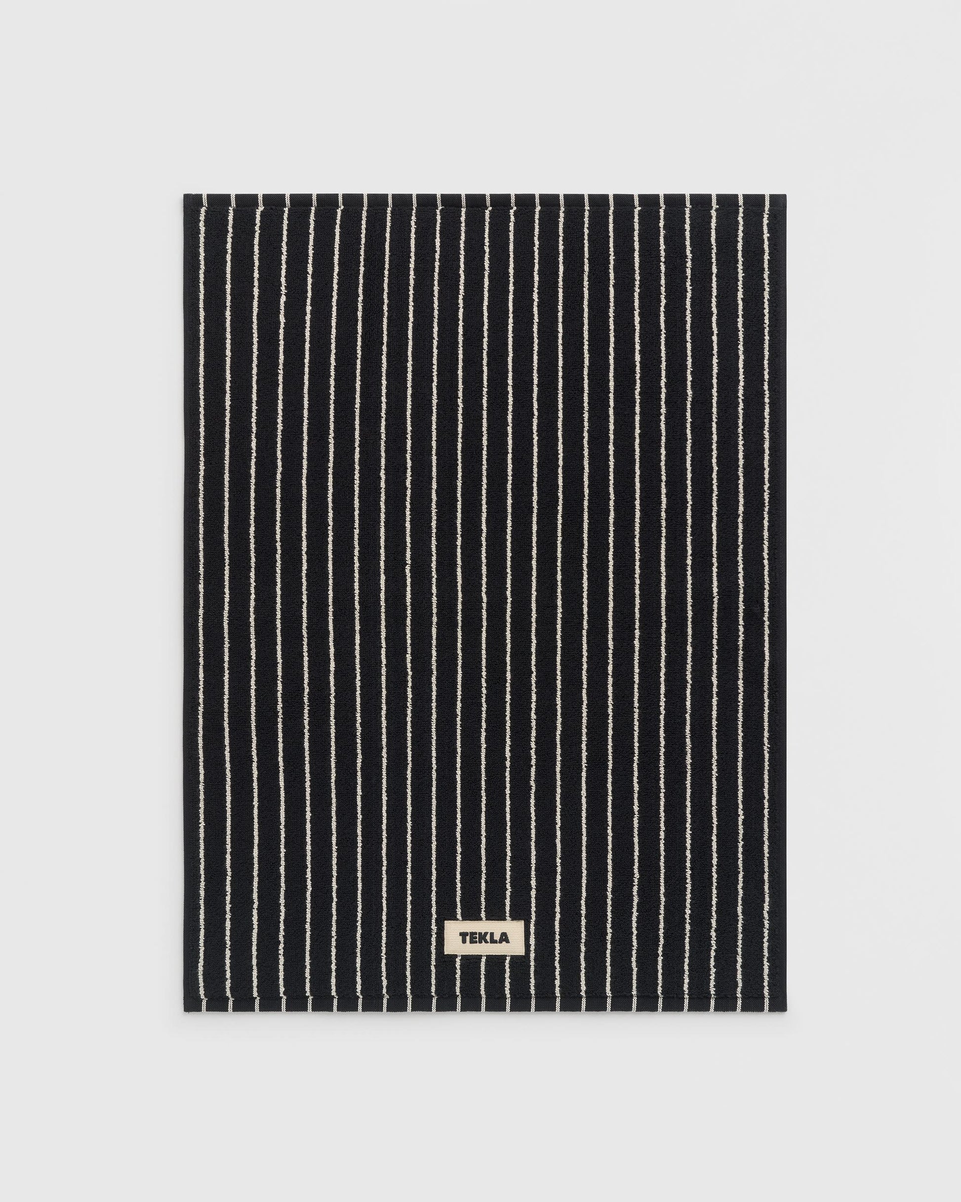 Black and white striped towel with 'Tekla' label on a light gray background