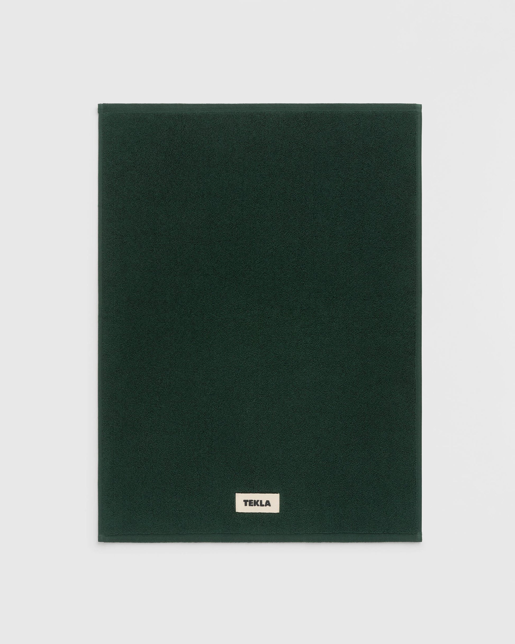 Dark green blanket with 'Tekla' label on a light gray background
