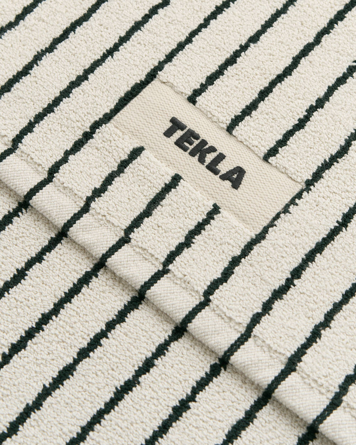 Textured fabric with black stripes and 'TEKLA' branding.