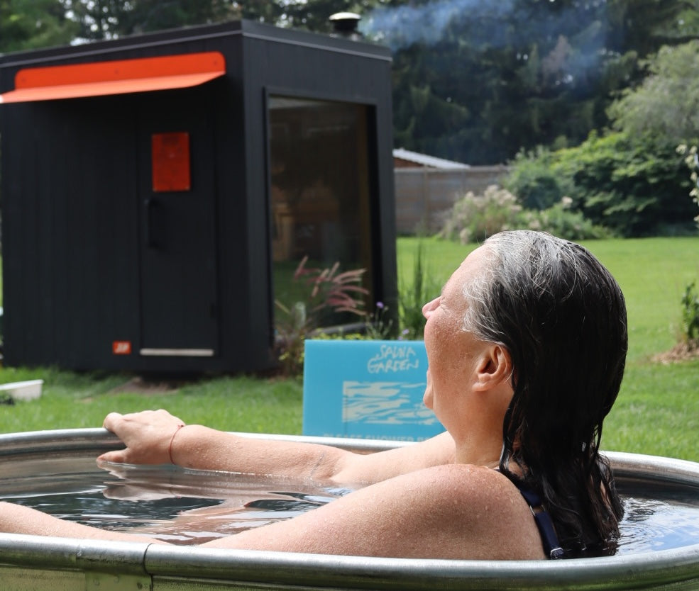 A guest relaxing in the cold plunge at the Sauna Garden, with the black Sip sauna behind