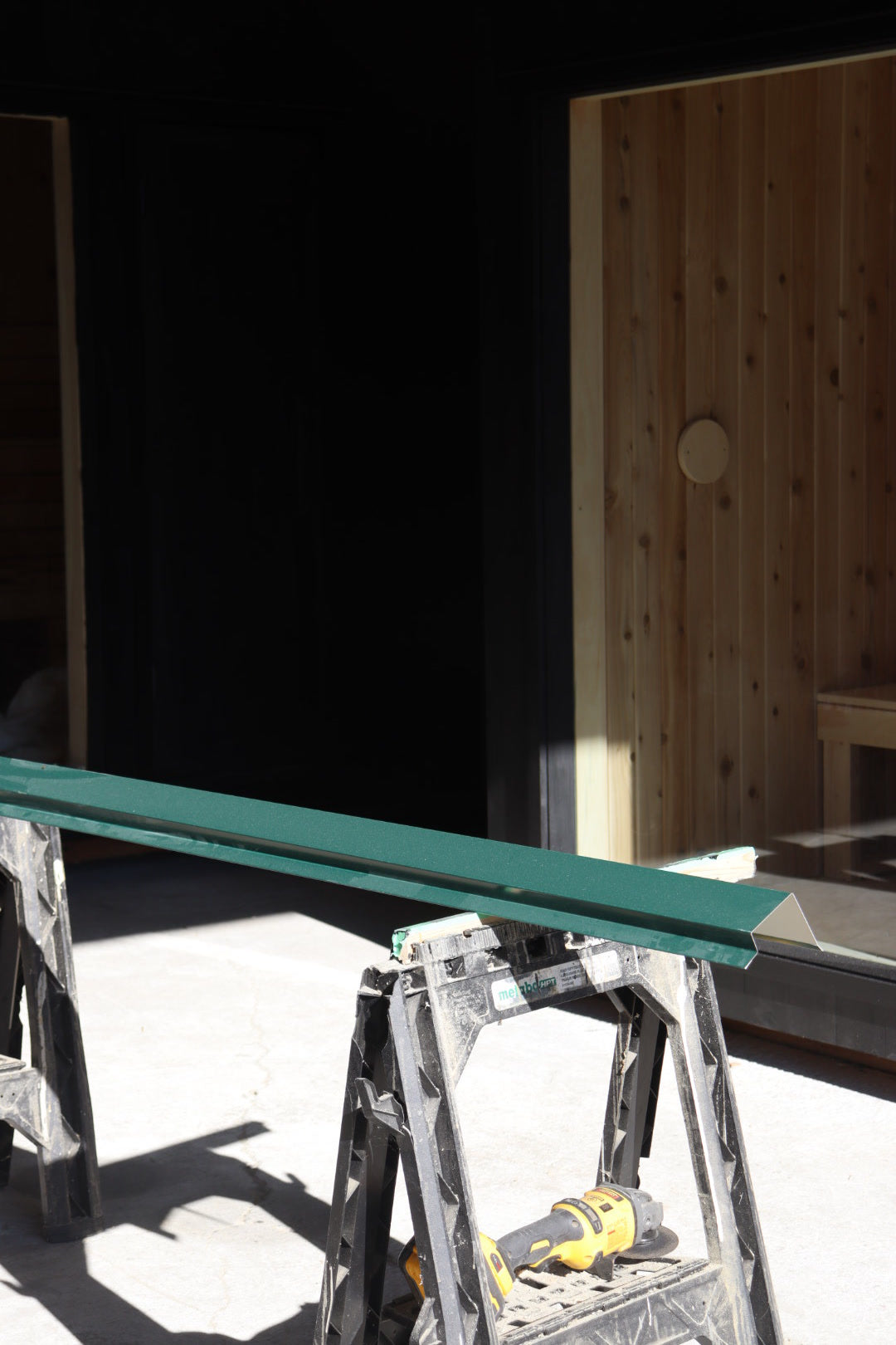 In the Sip Saunas shop: green metal flashing on sawhorses in front of a black sauna, cedar interior through the window